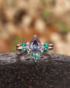 a ring with an amethorate and emeralds on it sitting on top of a rock