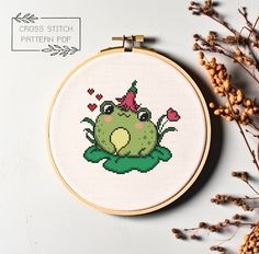 a cross stitch frog sitting on top of a plant