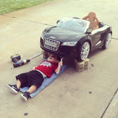 a little boy laying on the ground next to a toy car