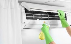 a person in green gloves and rubber gloves cleaning an air conditioner with a rag