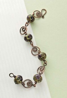 a close up of a bracelet on a white surface with green and purple glass beads