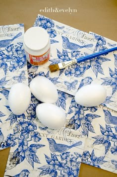 eggs and paint sitting on top of paper with blue floral designs next to each other