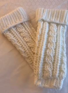 two white knitted arm warmers laying on top of a bed next to each other