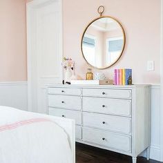 a white dresser sitting next to a bed in a room with pink walls and wooden floors