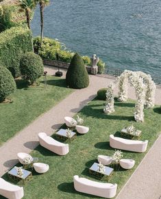 an outdoor wedding setup with white couches and flowers on the grass by the water