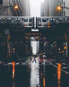 two people walking down the street in the rain under an overpass with traffic lights