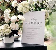 a memorial sign sitting on top of a table next to white flowers and greenery