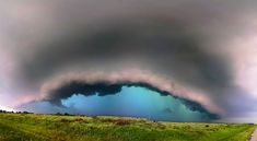 an image of a large storm coming in from the sky over a road and grassy field