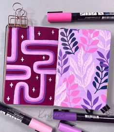 an open notebook with pink and purple designs on it, next to some marker pens