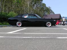 an old black car parked in a parking lot next to a person riding a bike