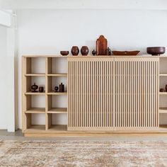 a wooden cabinet sitting on top of a rug in front of a wall mounted shelf filled with vases