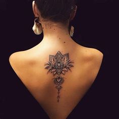 the back of a woman's neck with an intricate tattoo design on her lower back