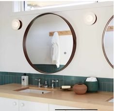 two round mirrors are above the sink in this bathroom with green tile and wood countertops