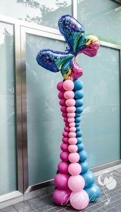 there is a tall balloon sculpture on the sidewalk with balloons attached to it and a butterfly sitting on top