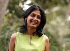 a woman in a green dress smiling at the camera with trees in the back ground