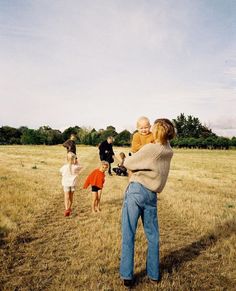 a group of people standing in a field with one holding a baby and the other carrying an infant