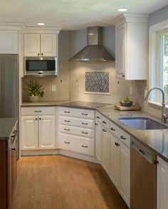 a clean kitchen with white cabinets and stainless steel appliances in the center, along with wooden floors