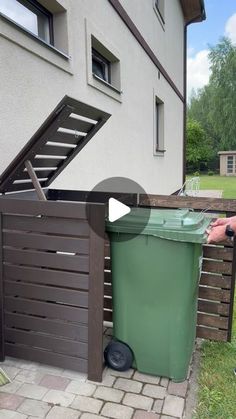 a man standing next to a green trash can on top of a brick floored yard