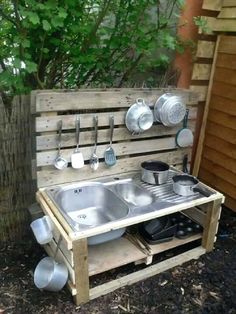 an outdoor sink made out of pallets and wooden crates with pots and pans hanging on the wall