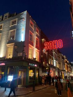 people are walking on the sidewalk in front of shops at night time with neon lights