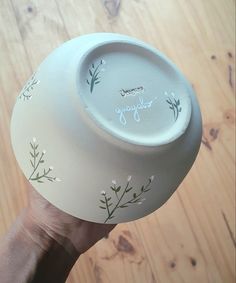 a hand holding a white bowl with flowers painted on it