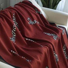 a red blanket with zebras on it sitting on a white chair in front of a potted plant