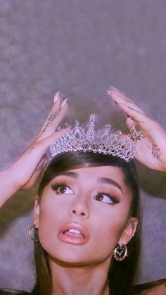 a woman wearing a tiara and holding her hands up to her head while looking at the camera