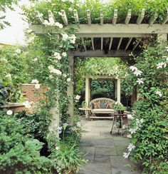 an outdoor seating area with white flowers and greenery on the arbor, surrounded by brick walls