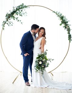 a bride and groom standing in front of a circular arch with greenery on it