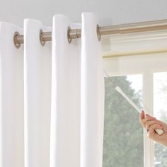 a woman is holding a paint roller in front of a window that has white curtains