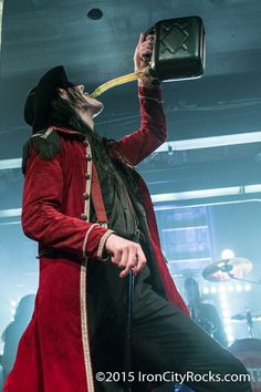 a man dressed in red and black with a hat on his head holding an object up to his mouth