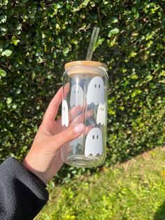 a hand holding a glass with some white ghost stickers on it and a green bush in the background