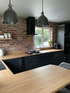 a kitchen with black cabinets and wooden counter tops, two pendant lights over the island