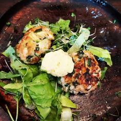 two crab cakes with greens and butter on a black plate, ready to be eaten