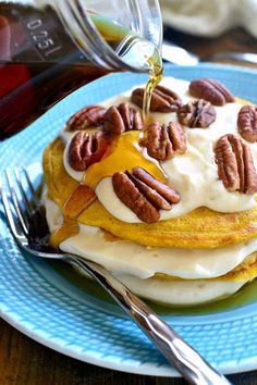 a blue plate topped with pancakes covered in frosting and pecans next to a fork