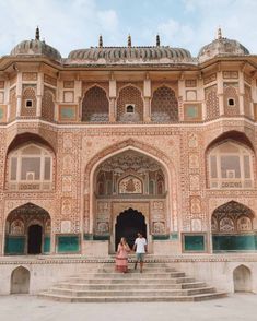 a man and woman standing in front of an ornate building with steps leading up to it