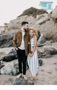 a man and woman standing next to each other on rocks near the ocean with a lifeguard tower in the background