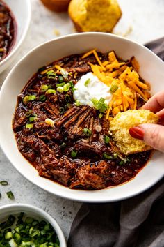 a bowl of chili with cornbreads, sour cream and cheese on the side