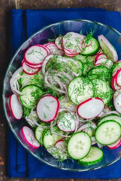 a bowl filled with sliced cucumbers and radishes on top of a blue cloth