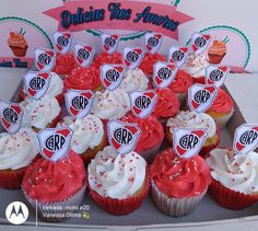 cupcakes with red and white frosting are arranged on a tray in front of a sign