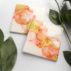 two marble coasters with gold and pink designs on them next to a green plant