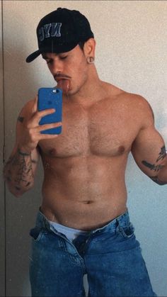 a shirtless man taking a selfie in the mirror with his cell phone and hat on