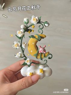 a hand holding a small figurine with flowers and a pig on the moon