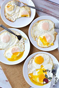 three white plates topped with eggs on top of a wooden table next to silverware