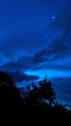 the sky is dark and blue at night with clouds in the foreground, some trees to the right