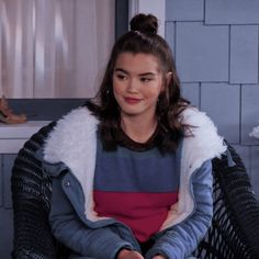 a young woman sitting on top of a chair in front of a window wearing a coat