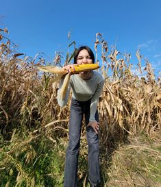 a woman holding a corn cob in front of her face while standing in a field