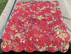 a red quilted blanket sitting on top of a bed in the middle of grass