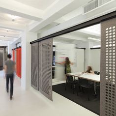 two people are walking through an office with large windows and doors on both sides of the room