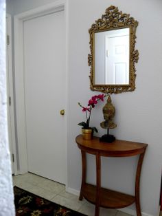 a table with a mirror and vase on it in front of a door that leads to another room